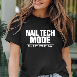 May include: Black t-shirt with the text "NAIL TECH MODE ALL DAY EVERY DAY" in white block letters. The shirt is a crew neck style and appears to be made of a soft material.