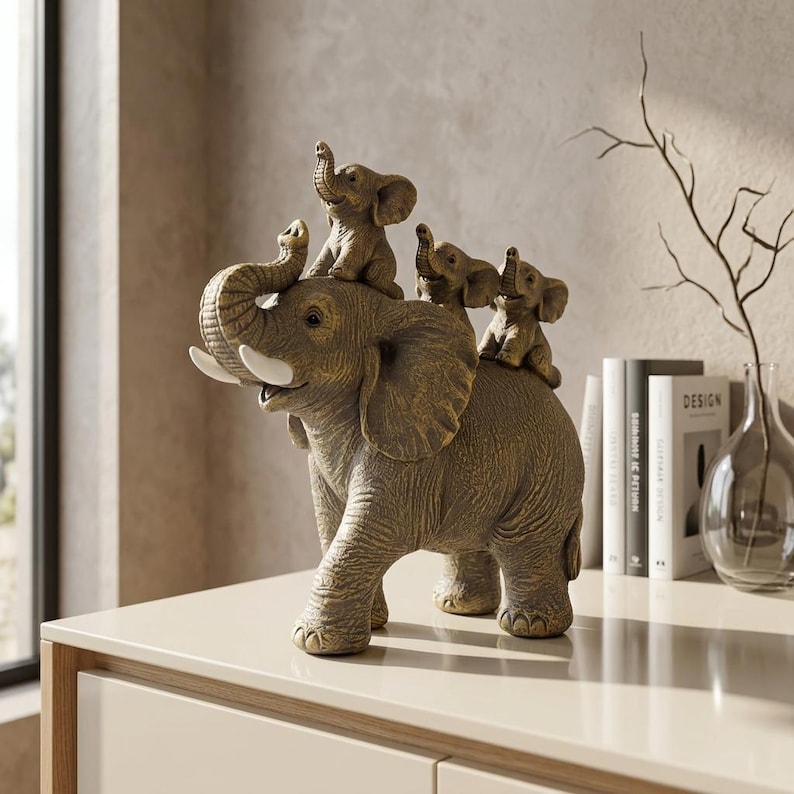 May include: A bronze-toned decorative figurine featuring a large adult elephant with white tusks and three smaller baby elephants perched on its back. The adult elephant has its trunk raised, and the baby elephants are depicted in various poses.