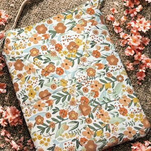 May include: A floral-patterned tote bag with a cream background and a repeating pattern of orange, yellow, and brown flowers and green leaves. The bag has a matching strap and is quilted. The bag is rectangular and has a handle.