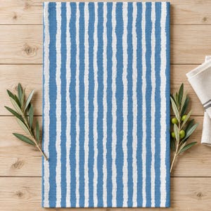 May include: A rectangular kitchen towel featuring a vertical striped pattern in alternating shades of blue and white. The stripes have a textured, hand-painted appearance with uneven, jagged edges. The fabric has a visible woven, waffle-like texture.