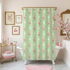 May include: A light green shower curtain with a repeating pattern of pink cocktail glasses, bows, and white polka dots. The curtain hangs in a bathroom with framed artwork and a pink heart-shaped rug.