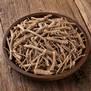 以下が含まれることがあります： 濃い茶色の木製ボウルに入った、乾燥した薄茶色の木質の根の断片。根は細く円筒形で、表面はざらざらとした質感があり、さまざまな長さと不規則な枝分かれのパターンが見られる。