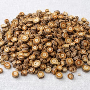 Peut inclure: Un grand tas de racines végétales séchées et tranchées. Chaque pièce circulaire présente une écorce extérieure texturée brun foncé et un intérieur jaune doré plus clair avec un motif radial en forme d'étoile au centre de la coupe.