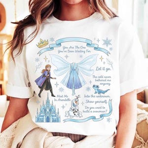 May include: White t-shirt featuring illustrations and text from a popular animated movie. The design includes a crown, snowflakes, a castle, and characters. Text includes phrases like "You Are The One" and "Let it go."