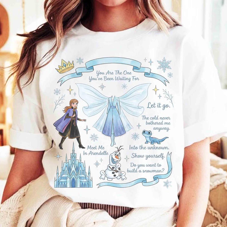 May include: White t-shirt featuring illustrations and text from a popular animated movie. The design includes a crown, snowflakes, a castle, and characters. Text includes phrases like "You Are The One" and "Let it go."