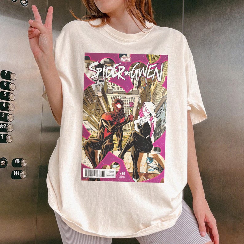 Puede incluir: Camiseta color crema con la portada del c&oacute;mic "Spider-Gwen". El arte del c&oacute;mic muestra a dos superh&eacute;roes disfrazados contra un paisaje urbano. La camiseta tiene cuello redondo y mangas cortas.