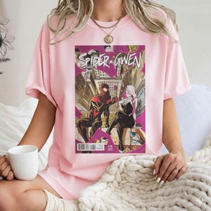 Puede incluir: Camiseta rosa claro con una portada de c&oacute;mic "Spider-Gwen". El arte del c&oacute;mic muestra dos figuras disfrazadas en un entorno urbano. La camiseta es una prenda casual.