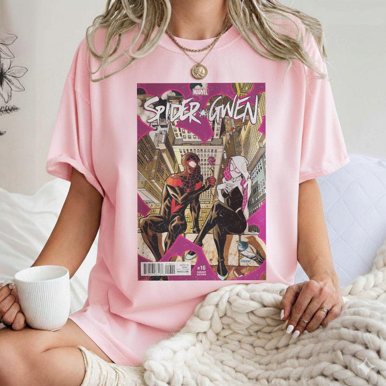 Puede incluir: Camiseta rosa claro con una portada de c&oacute;mic "Spider-Gwen". El arte del c&oacute;mic muestra dos figuras disfrazadas en un entorno urbano. La camiseta es una prenda casual.