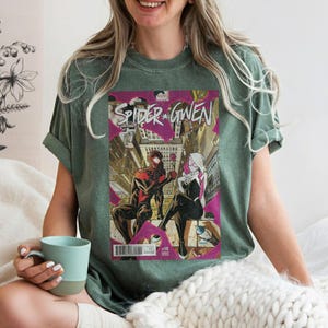 Puede incluir: Camiseta verde con una portada de c&oacute;mic de "Spider-Gwen". El arte del c&oacute;mic muestra a dos Spider-People en un entorno urbano. La camiseta tiene mangas cortas y cuello redondo.