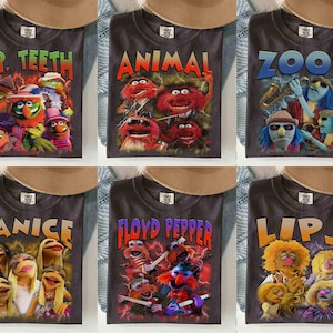 May include: Six dark gray t-shirts featuring Muppet characters and their names in colorful text. The shirts include Dr. Teeth, Animal, Zoot, Janice, Floyd Pepper, and Lips. Each shirt has a vintage, distressed design.
