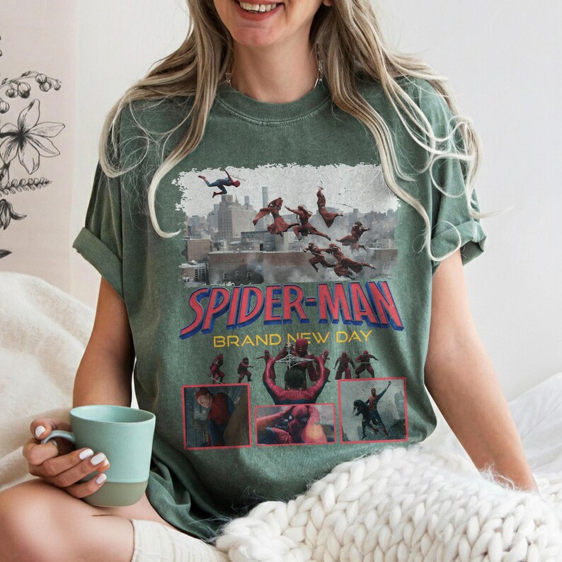 May include: A green t-shirt featuring a Spider-Man graphic with the text "SPIDER-MAN BRAND NEW DAY". The graphic depicts Spider-Man in action with a cityscape background. The shirt is a relaxed fit.