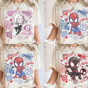 May include: Four cream-coloured t-shirts featuring Spider-Man characters. Each shirt has a unique design with the words "AMAZING" and a character name, along with comic-style illustrations of Spider-Man, Gwen, and Miles.