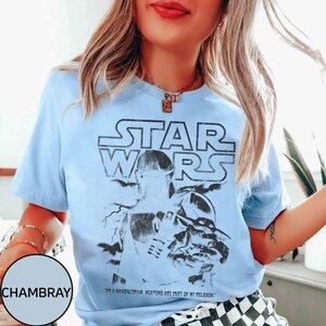 Puede incluir: Camiseta azul claro con un gr&aacute;fico de Star Wars con The Mandalorian. El dise&ntilde;o incluye el logotipo de Star Wars y el texto "I'm a Mandalorian. Weapons are part of my religion."