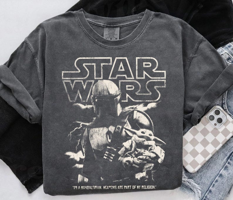 Puede incluir: Camiseta gr&aacute;fica gris oscuro de Star Wars con The Mandalorian y Grogu. La camiseta tiene el logo de Star Wars en blanco, con el texto "I'M A MANDALORIAN. WEAPONS ARE PART OF MY RELIGION." impreso debajo.