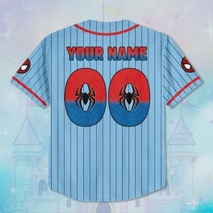 Puede incluir: Camiseta de b&eacute;isbol azul claro con detalles rojos y azules. La parte trasera presenta el texto "YOUR NAME" en rojo y azul, junto con dos c&iacute;rculos rojos y azules con un gr&aacute;fico de ara&ntilde;a y el n&uacute;mero "00". Logotipo de Spider-Man en las mangas.