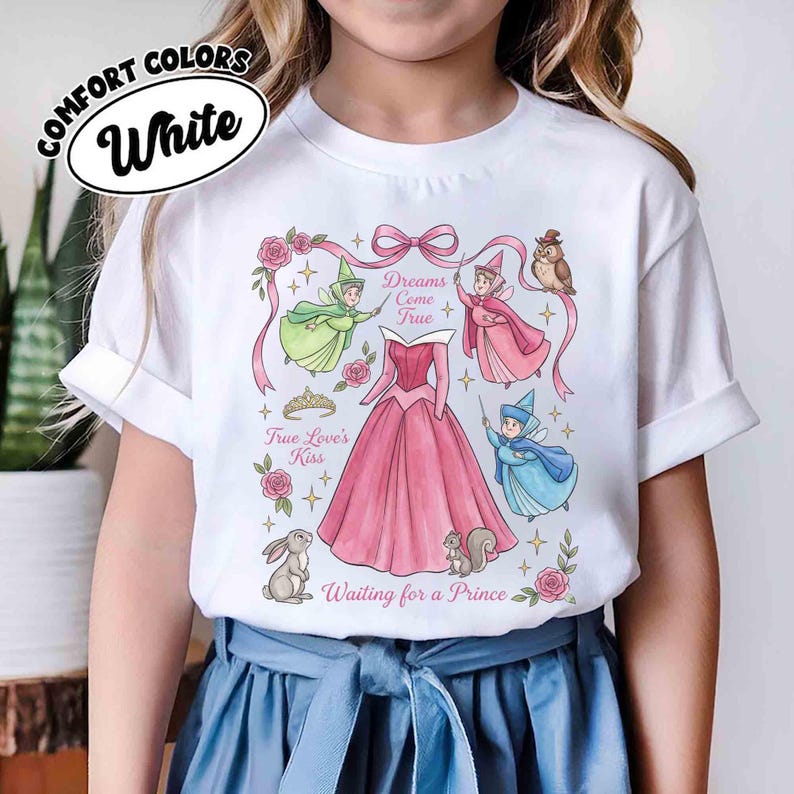 May include: White t-shirt featuring a pink princess dress design with fairies, an owl, and the text "Dreams Come True" and "Waiting for a Prince." The shirt also has the text "True Love's Kiss."