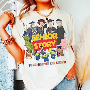 K&ouml;nnte beinhalten: Cremefarbenes T-Shirt mit einer farbenfrohen Grafik von Zeichentrickfiguren in Abschlusskleidung. Der Text "SENIOR STORY" ist in gro&szlig;en, fetten Buchstaben dargestellt, darunter "TO GRADUATION AND BEYOND". Das Design umfasst verschiedene Charaktere.