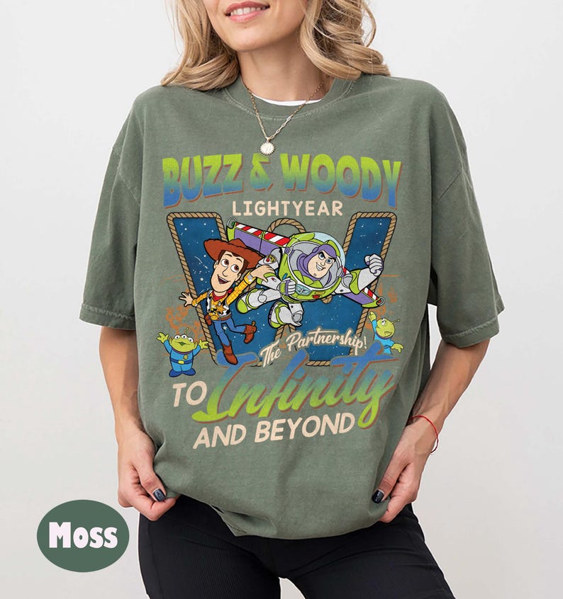 May include: Moss green t-shirt featuring a graphic of Buzz Lightyear and Woody from Toy Story. The design includes the text "Buzz & Woody Lightyear" and "To Infinity and Beyond". The shirt is a relaxed fit.