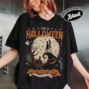 May include: Black t-shirt with a Halloween-themed graphic. The design features a full moon, silhouettes of figures, bats, ghosts, pumpkins, and the text "THIS IS HALLOWEEN". The phrase "EVERYBODY MAKE A SCENE!" is on a banner below the pumpkins.