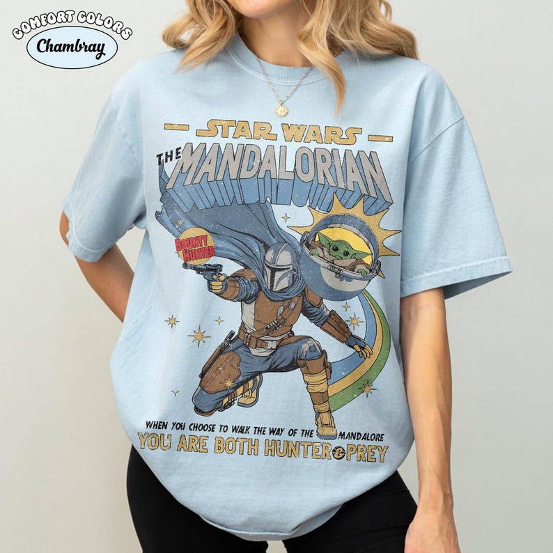 以下が含まれることがあります： スターウォーズのマンダロリアンが描かれたライトブルーのTシャツ。「STAR WARS - THE MANDALORIAN」と「WHEN YOU CHOOSE TO WALK THE WAY OF THE MANDALORE YOU ARE BOTH HUNTER & PREY」の文字が含まれています。