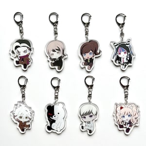 Może przedstawiać: Osiem akrylowych breloków do kluczy z postaciami w stylu anime. Każdy brelok ma srebrny pierścień i łańcuszek. Postacie są w różnych pozach i strojach, z różnymi kolorami i stylami włosów. Breloki znajdują się na białym tle.