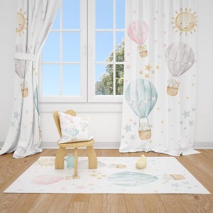 May include: A nursery decor set featuring a white rug, curtains, and a pillow, all adorned with watercolor illustrations of hot air balloons, stars, and smiling suns. A small wooden chair and a yellow pear-shaped toy are also present.