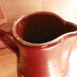 May include: A brown ceramic pitcher with a chipped rim and a handle. The pitcher is empty and has a worn, rustic look.