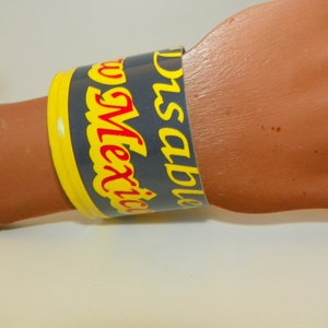 May include: A blue and yellow paper bracelet with the text "Disposable New Mexico" in red.