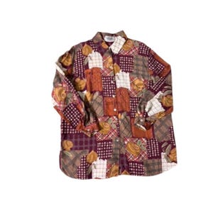 Può includere: Una camicia abbottonata a maniche lunghe con un design patchwork. La camicia presenta un mix di motivi, tra cui quadrati floreali, a quadri e a tinta unita in tonalità bordeaux, marrone, arancione e crema. Il colletto e i polsini sono visibili.