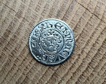 May include: A circular silver-toned coin featuring a central embossed portrait of a bearded figure wearing a crown. The coin displays intricate lettering around the perimeter and a cross-topped staff held by the figure on the left side.