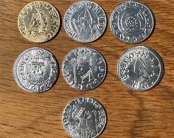 May include: Seven antique coins of various designs and sizes are arranged on a wooden surface. One coin is gold, while the others are silver-toned. The coins feature portraits, symbols, and inscriptions, showcasing historical craftsmanship.