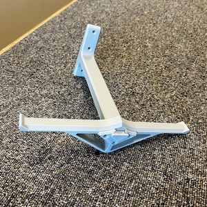 May include: A light gray plastic bracket with a light blue accent. The bracket has a triangular base and two horizontal arms. The bracket is designed to hold an object. The bracket is made of plastic.