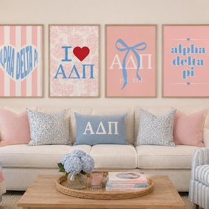 May include: Four framed wall art prints featuring Alpha Delta Pi sorority themes in pink and blue. The prints include a heart with text, an I heart ADPi design, a blue bow with Greek letters, and text reading alpha delta pi with small hearts.