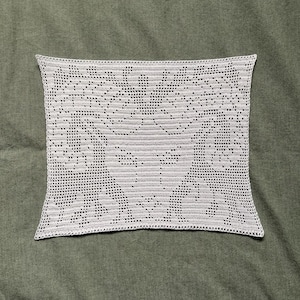 Peut inclure: Nappe rectangulaire en crochet gris clair avec un motif floral détaillé. La nappe est faite d'un fil doux et texturé et est présentée sur une surface verte. Le crochet présente des motifs ajourés.