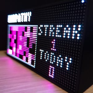 K&ouml;nnte beinhalten: Eine wei&szlig;e Keramik-Tasse mit schwarzem Henkel und dem Text "But First, Coffee" in fetter, schwarzer Schrift. Die Tasse steht vor einem verschwommenen Hintergrund, der eine gem&uuml;tliche Umgebung suggeriert.