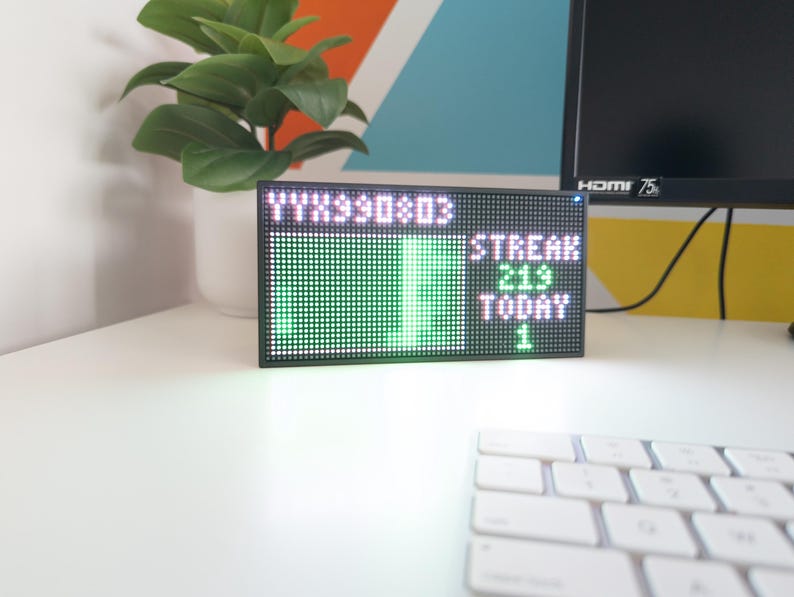 K&ouml;nnte beinhalten: Ein schwarzer LED-Bildschirm mit gr&uuml;nem und wei&szlig;em Text und Grafiken. Der Bildschirm zeigt die W&ouml;rter "STREAK 219 TODAY 1". Eine wei&szlig;e Tastatur befindet sich im Vordergrund. Eine Topfpflanze befindet sich im Hintergrund.