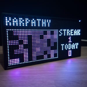 K&ouml;nnte beinhalten: Schwarzes rechteckiges LED-Display mit wei&szlig;en und lila Lichtern. Das Display zeigt das Wort "KARPATHY" oben und die Zahlen "37:33" in der Mitte. Die W&ouml;rter "STREAM", "1", "TODAY" und "0" werden ebenfalls angezeigt.