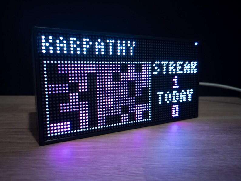 K&ouml;nnte beinhalten: Schwarzes rechteckiges LED-Display mit wei&szlig;en und lila Lichtern. Das Display zeigt das Wort "KARPATHY" oben und die Zahlen "37:33" in der Mitte. Die W&ouml;rter "STREAM", "1", "TODAY" und "0" werden ebenfalls angezeigt.