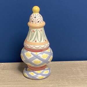 May include: A decorative ceramic salt shaker with a yellow top and base. The body is painted with a light blue and yellow crisscross pattern. The middle section has a floral design with pink and green accents.