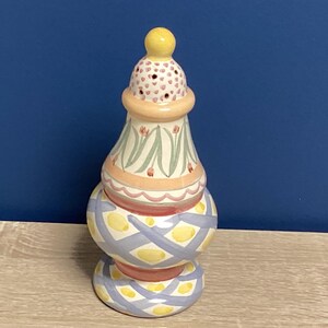 May include: A decorative ceramic vase with a yellow finial. The vase features a stacked design with painted floral and geometric patterns in pastel colors, including pink, blue, and yellow. The vase is approximately 8 inches tall.