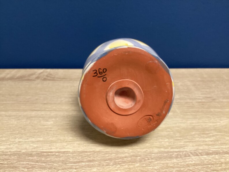 May include: A ceramic, cylindrical object with a rounded base. The exterior features a blue and white pattern with yellow accents. The base is reddish-brown with a central hole. The number "360" is written on the side.