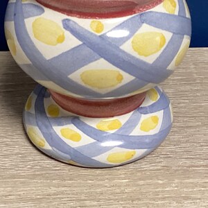 May include: A ceramic decorative item with a bulbous top and a circular base. The item is painted with a white background, blue crisscross pattern, and yellow oval shapes. The center is red.