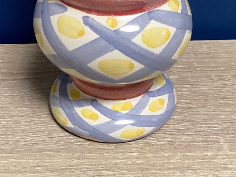 May include: A ceramic decorative item with a bulbous top and a circular base. The item is painted with a white background, blue crisscross pattern, and yellow oval shapes. The center is red.