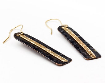 May include: A pair of long, black and gold earrings with a hammered texture. The earrings have a simple, modern design.