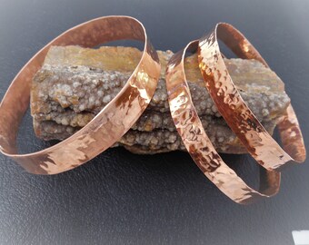 May include: Three hammered copper bangles stacked on a piece of brown and white rock.