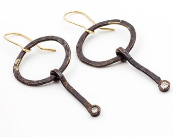 May include: A pair of hammered metal earrings with a circular design and a dangling diamond accent. The earrings are made of oxidised silver and have a gold-tone hook.
