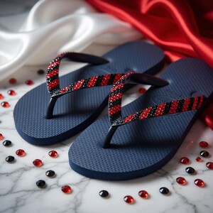 Peut inclure: Tongs bleu marine avec des lani&egrave;res noires orn&eacute;es de strass rouges et noirs. Les sandales sont pr&eacute;sent&eacute;es sur une surface en marbre avec des pierres pr&eacute;cieuses rouges et noires &eacute;parpill&eacute;es, et un tissu satin&eacute; rouge et blanc en arri&egrave;re-plan.