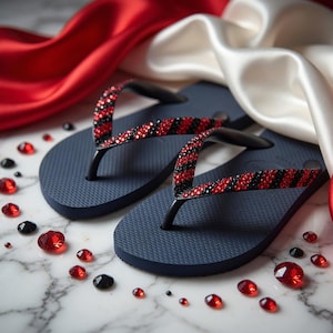 Peut inclure: Une paire de tongs bleu marine avec des lani&egrave;res orn&eacute;es de strass rouges et noirs altern&eacute;s. Des pierres pr&eacute;cieuses rouges et noires sont dispers&eacute;es autour des sandales, sur un fond de tissu de satin rouge et blanc.
