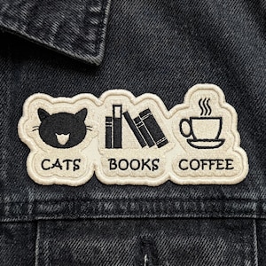 May include: Embroidered patch featuring a black cat, books, and a coffee cup with steam. The words "CATS", "BOOKS", and "COFFEE" are embroidered below each image. The patch is on a dark denim jacket.