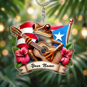 May include: A keychain featuring a brown frog playing a guitar, with the Puerto Rican flag in the background. The frog has red eyes and is surrounded by red hibiscus flowers. A banner below reads "Your Name".